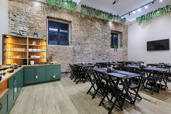 Un comedor con mesas y sillas de madera, una pared de piedra y una repisa con cristalería y vajilla.