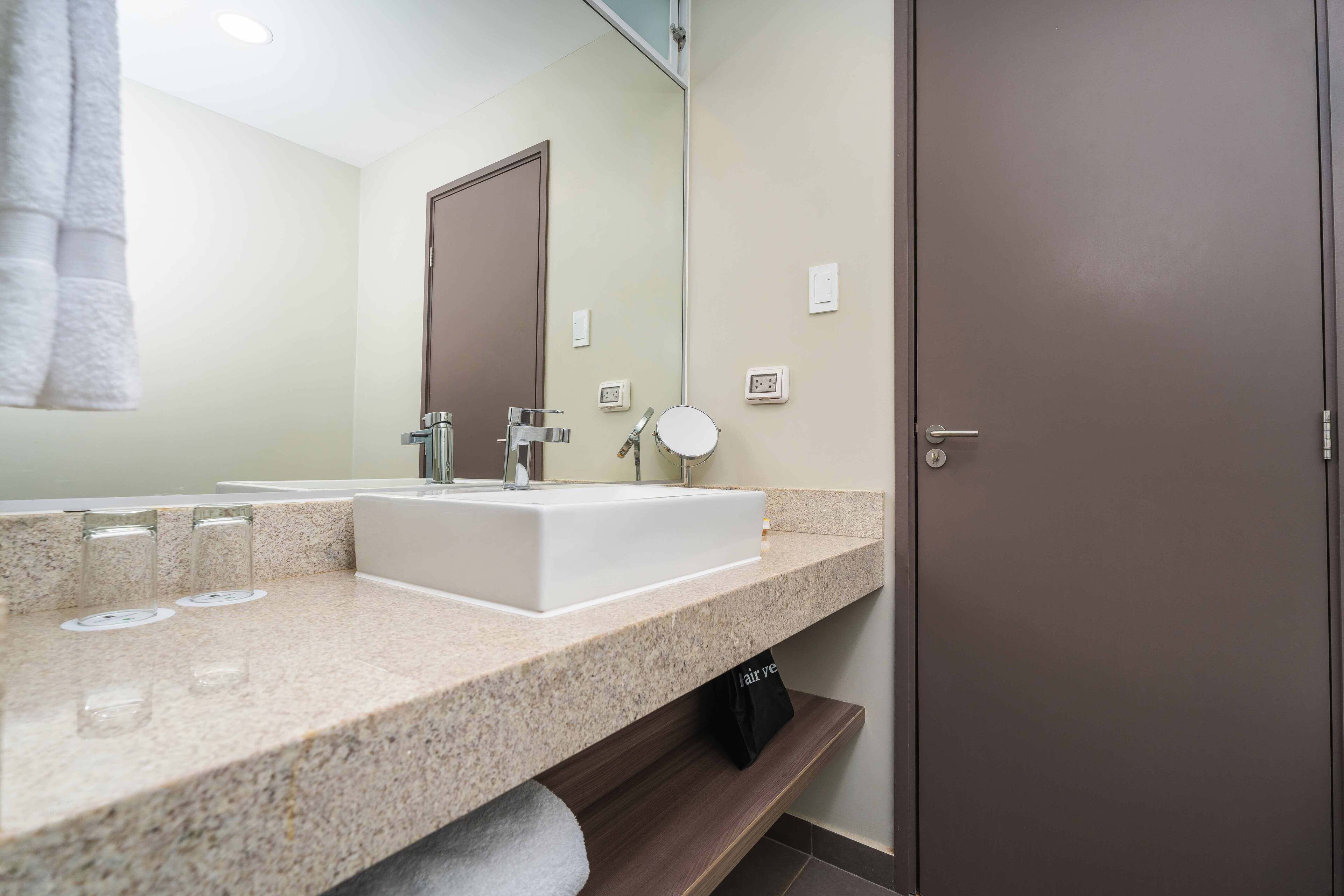 Un baño moderno con un espejo grande, un lavabo blanco y un perchero para toallas.