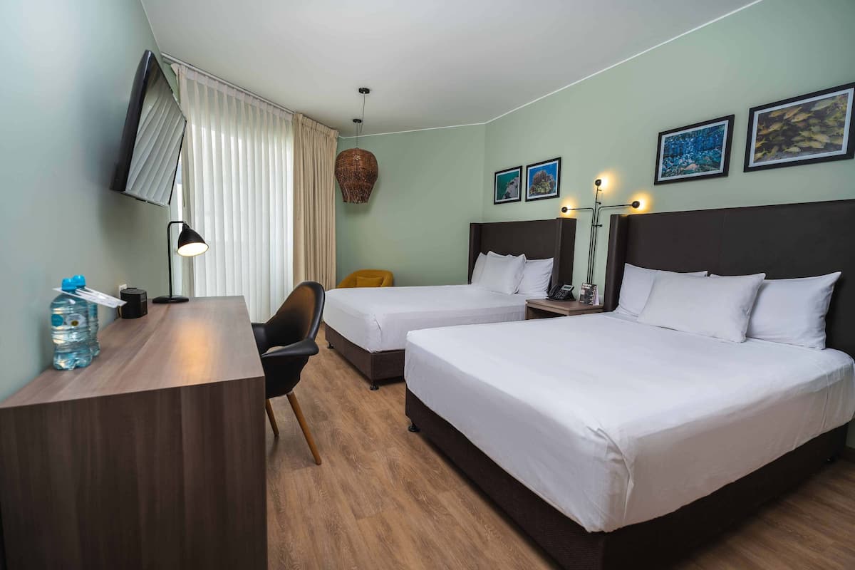 A hotel room with two beds, a desk, a chair, a lamp, and artwork on the walls.
