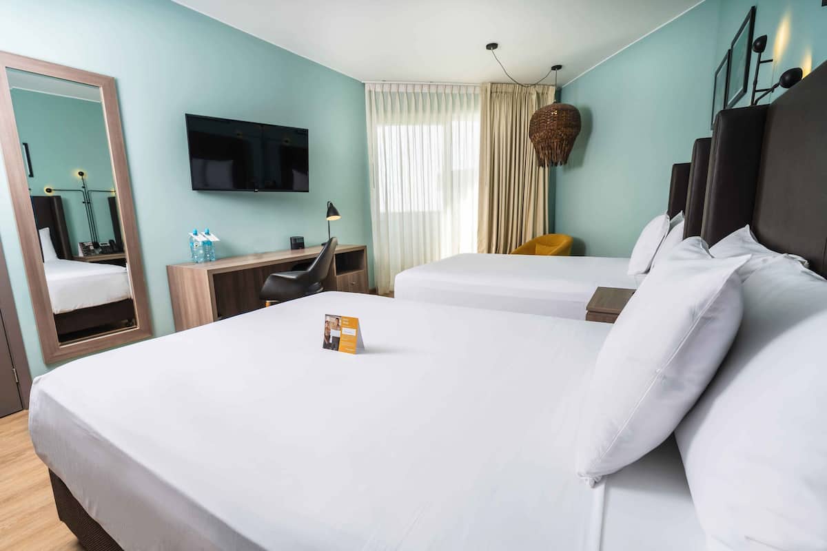 A hotel room with two beds, a desk, a TV, and a mirror.