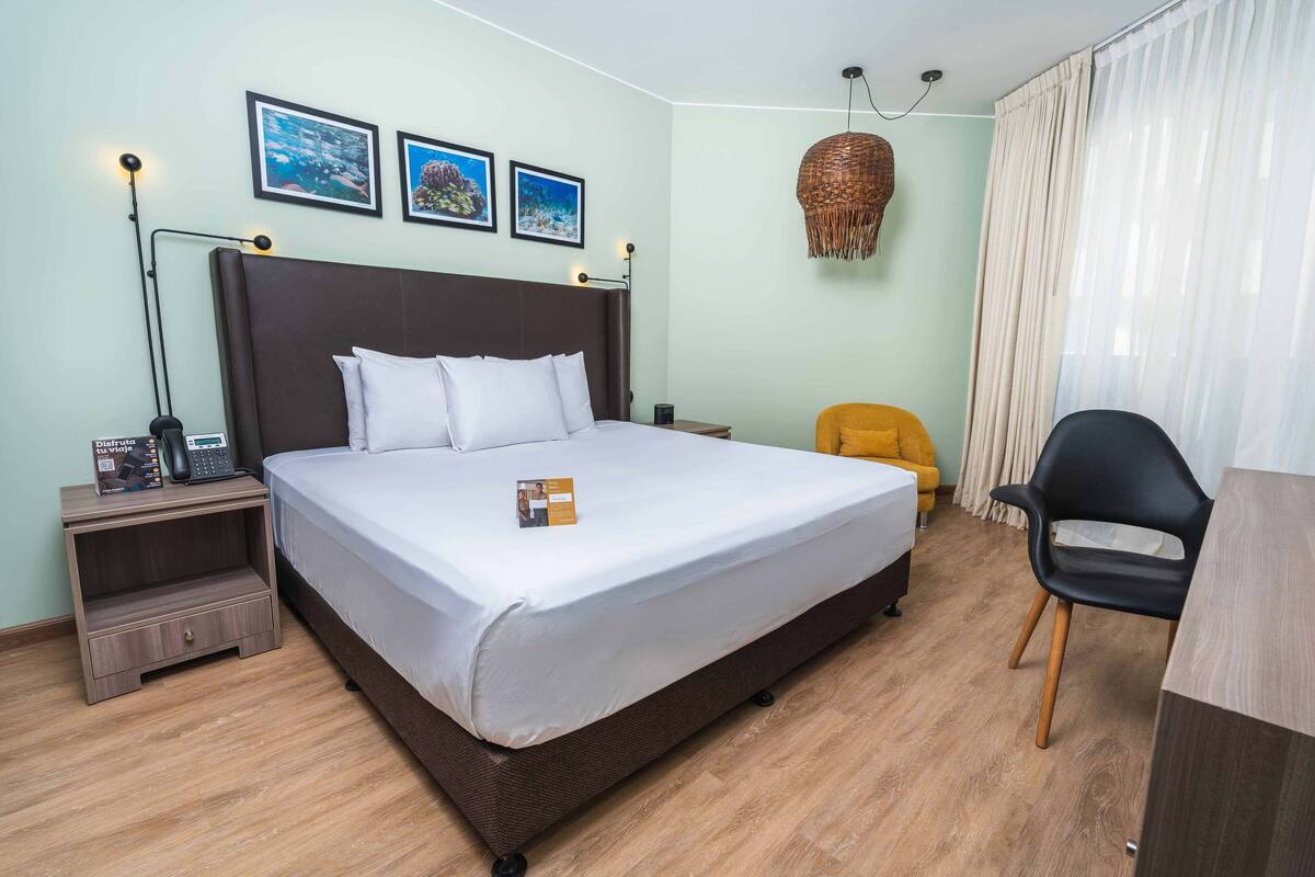 A neatly arranged hotel room with a large bed, a bedside table with a lamp, a chair, and a small table.
