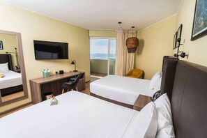 Habitación de hotel con dos camas, un escritorio, un televisor y un balcón con vistas.