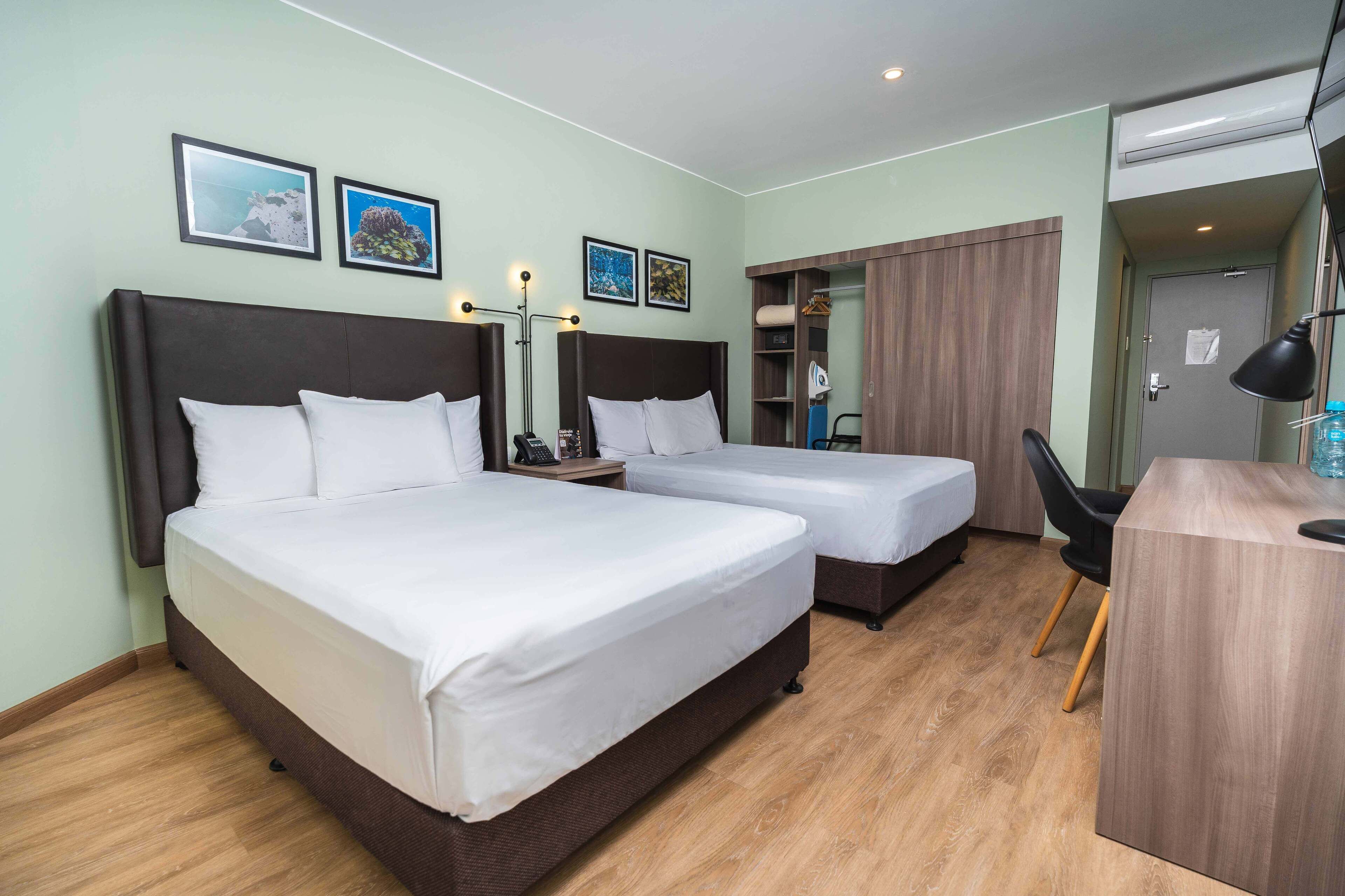 Quarto de hotel com duas camas, uma escrivaninha, uma cadeira e um guarda-roupa.