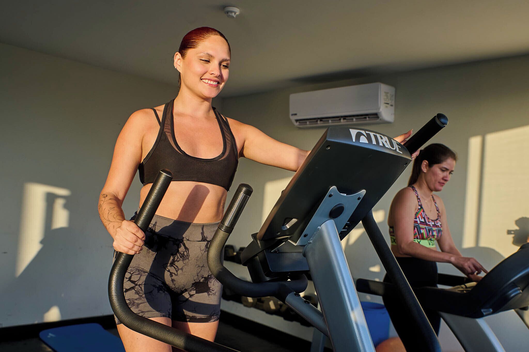 Ginásio com equipamentos de exercício e uma pessoa a correr numa esteira.