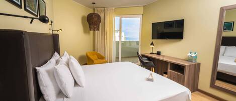 Habitación de hotel con una cama grande, un escritorio, una silla, un televisor y un balcón con vistas.
