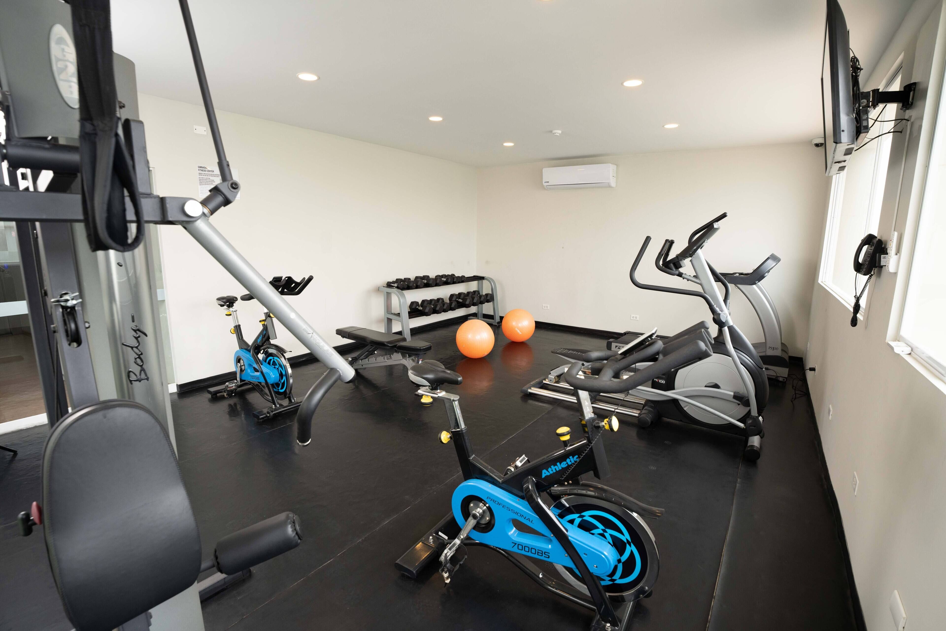 Un gimnasio con equipo de ejercicio, que incluye una bicicleta estática, elíptica y pesas.
