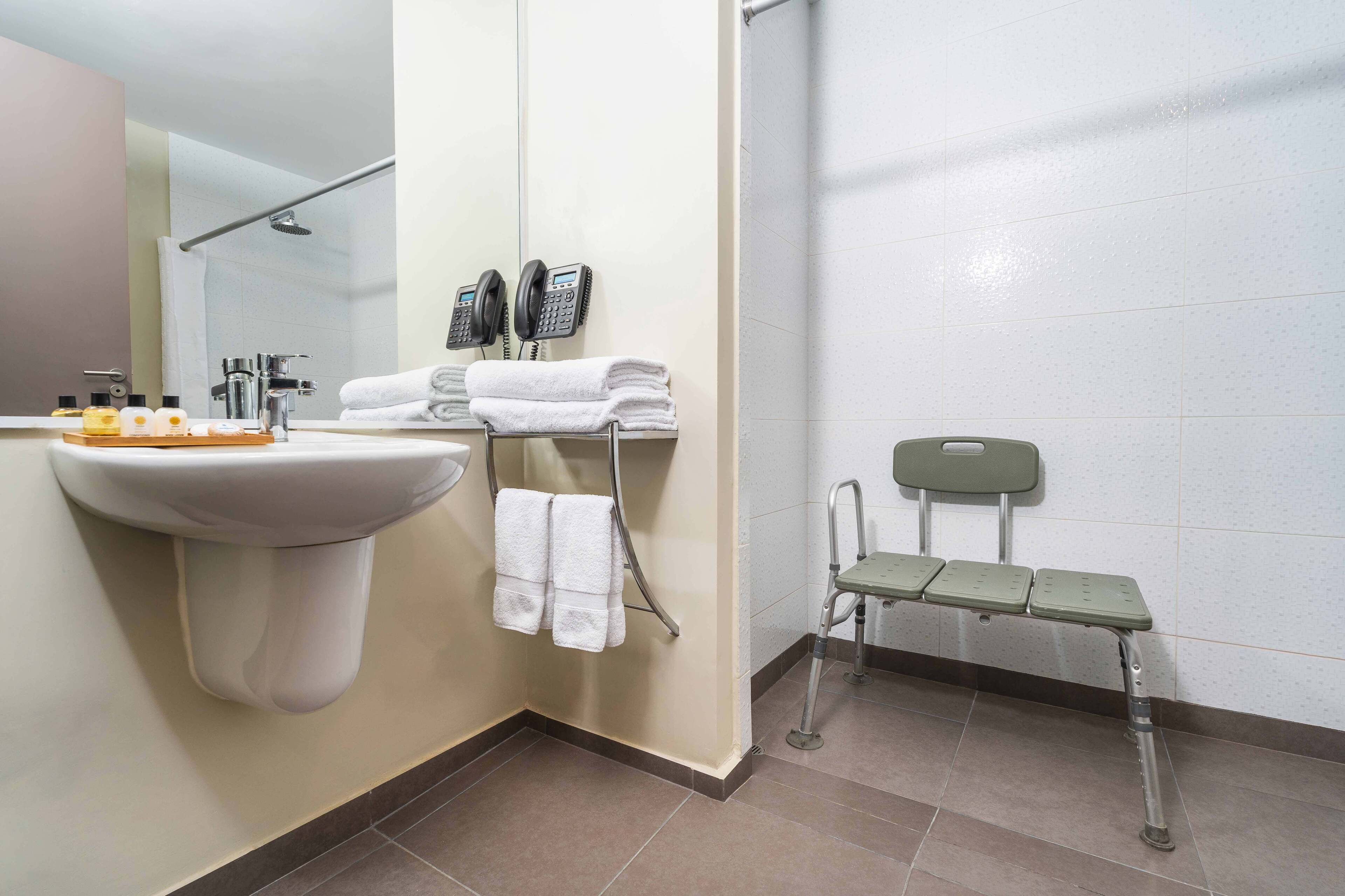 A bathroom with a sink, two phones, a towel rack, and a bench.