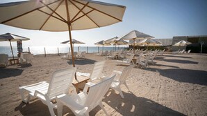 A beach with white plastic lounge chairs and umbrellas, arranged in rows. - Casa Andina Select Paracas (Paracas)