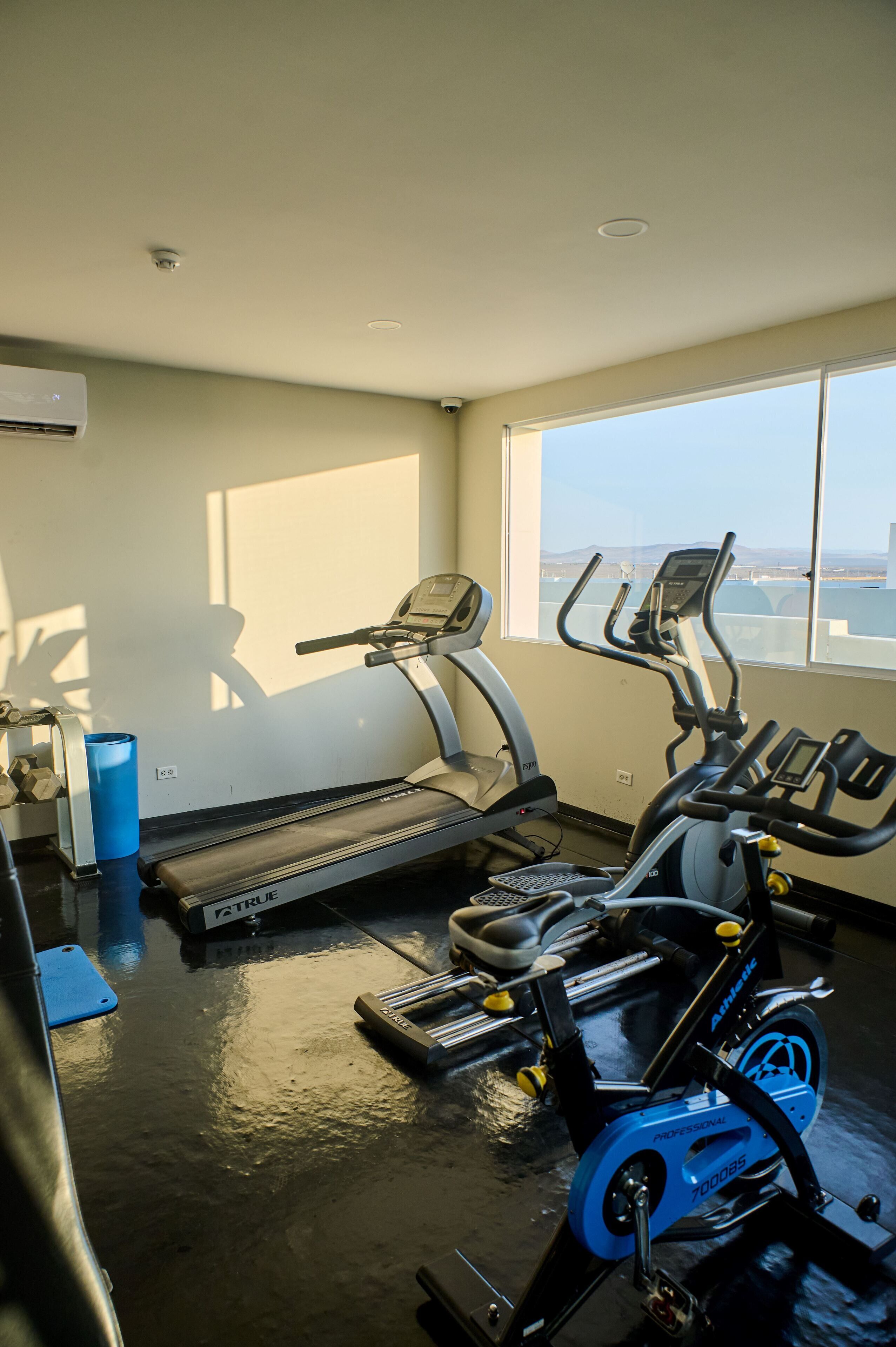 A gym with exercise equipment, a window with a view, and a blue water bottle on the floor.