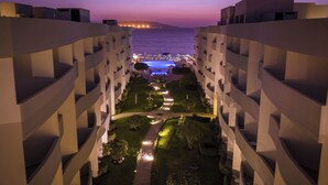 Une cour d’hôtel au crépuscule, avec une piscine et un espace détente, entourée d’immeubles modernes.