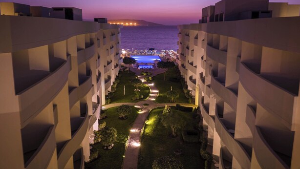 A hotel courtyard at dusk with a pool and lounge area, surrounded by modern buildings. - Casa Andina Select Paracas (Paracas)