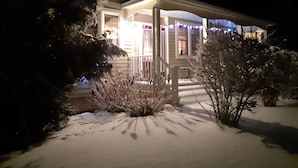 A snow-covered house with a porch and a snow-covered bush.