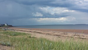 A beach with a lighthouse, grassy dunes, and a cloudy sky.