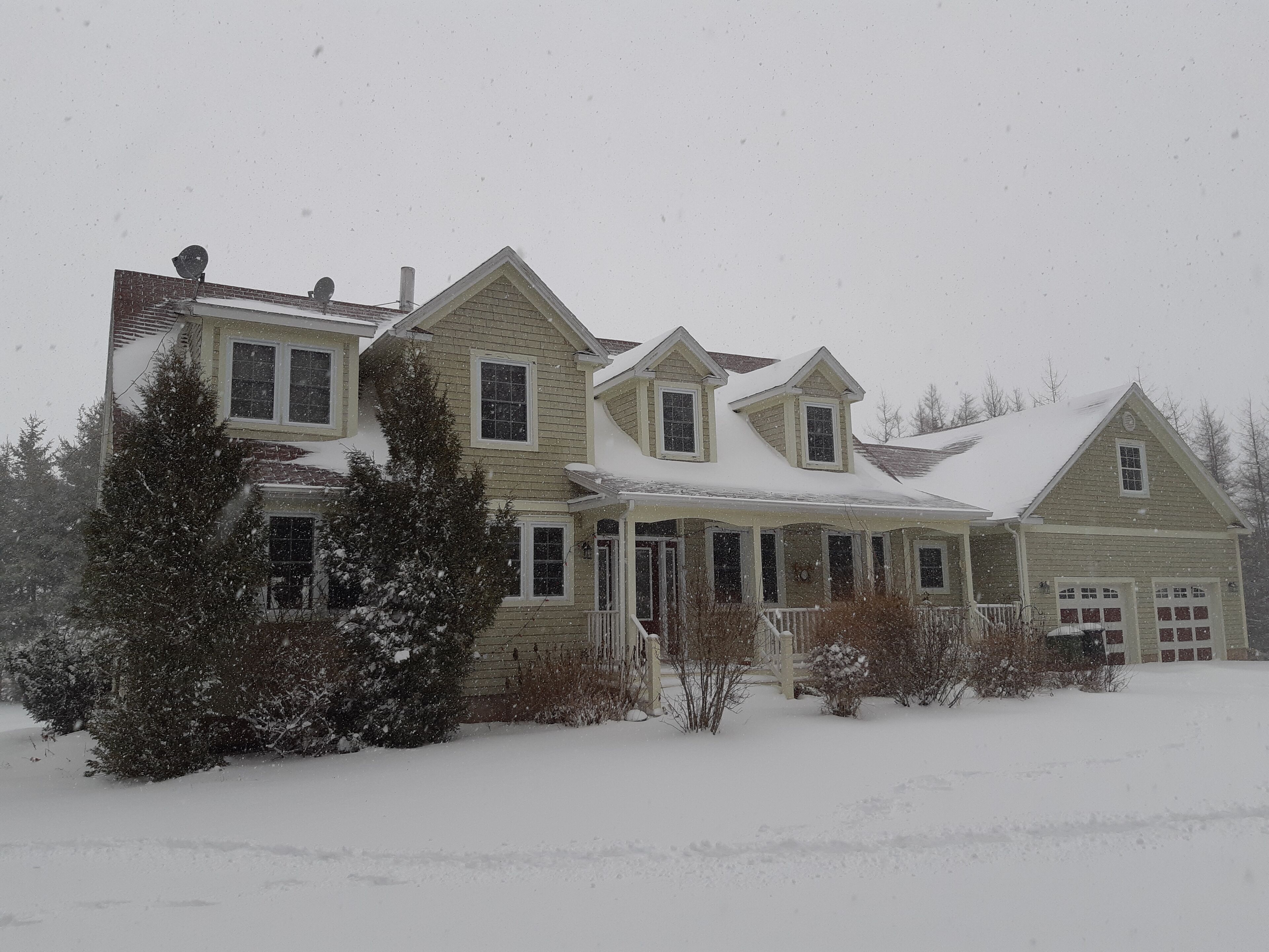 A two-story house with a porch and a garage, surrounded by snow.