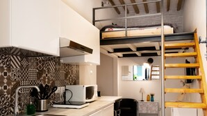 A compact kitchen with a built-in microwave, a sink, and a wooden loft bed. - The nest - Cozy studio apartment in Santa Croce (Firenze)