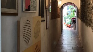 A narrow hallway with tiled flooring, framed artworks on the walls, and a doorway leading to an outdoor area with potted plants. - The nest - Cozy studio apartment in Santa Croce (Firenze)