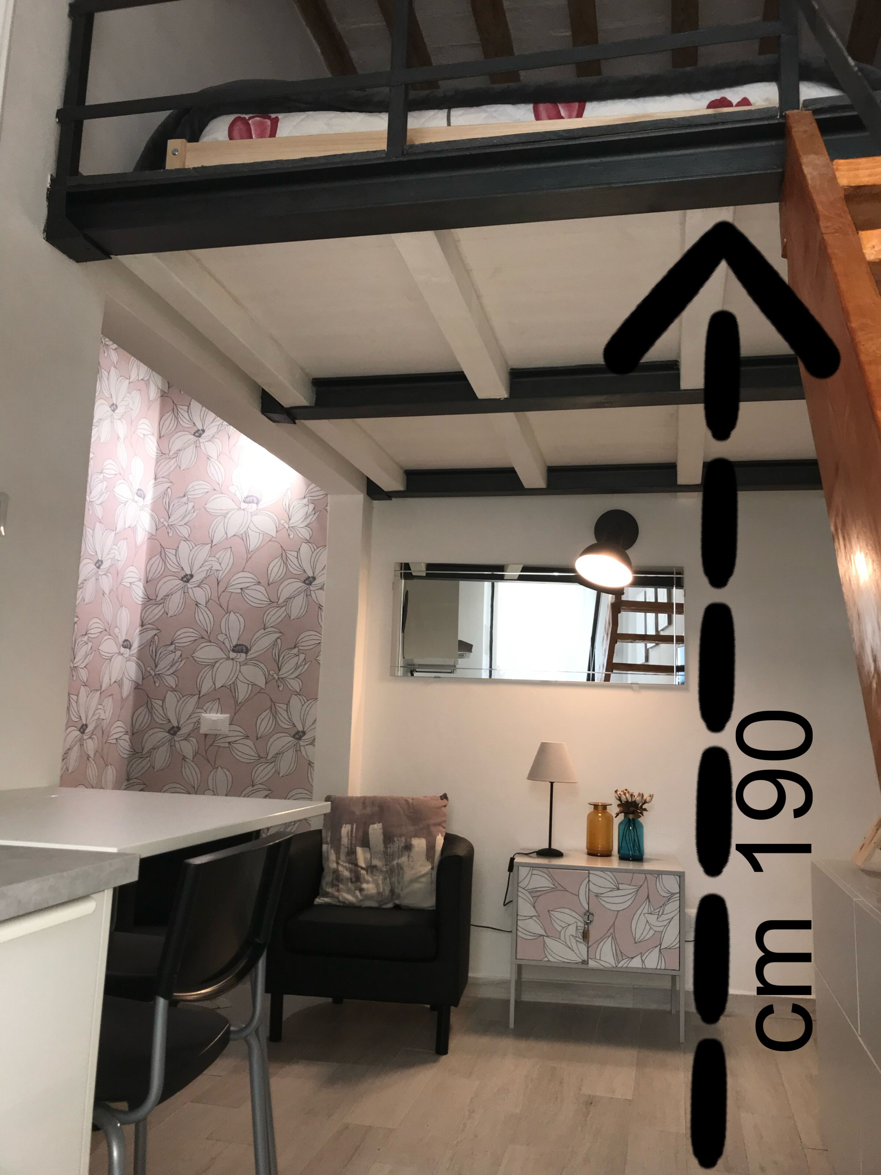 A modern kitchen with a dining area, a black sofa, and a staircase with a wooden railing.
