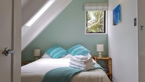 Un dormitorio con una cama, una ventana con vistas a árboles, una lámpara de noche y una pila de toallas.