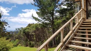 Una escalera de madera conduce a una cabaña con vistas a un espacio cubierto de césped y árboles.