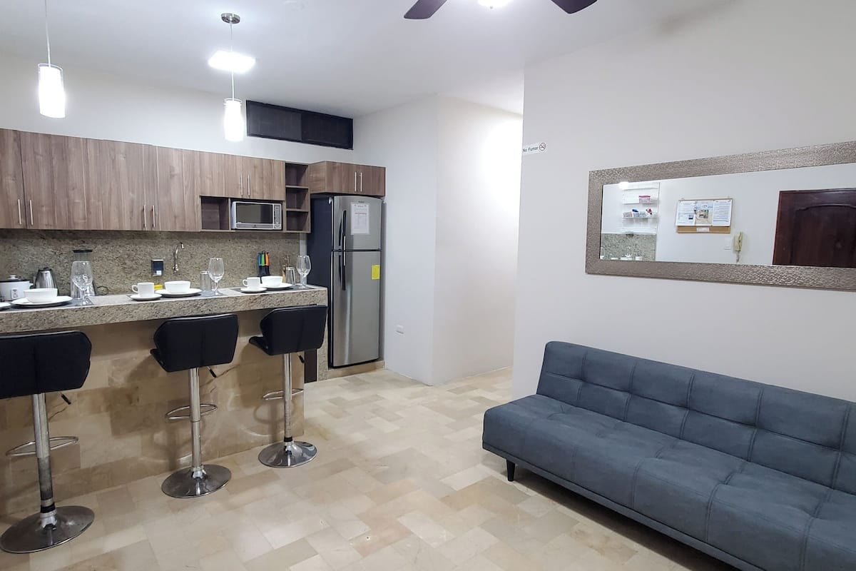 A modern kitchen with a microwave, refrigerator, bar stools, and a blue sofa.