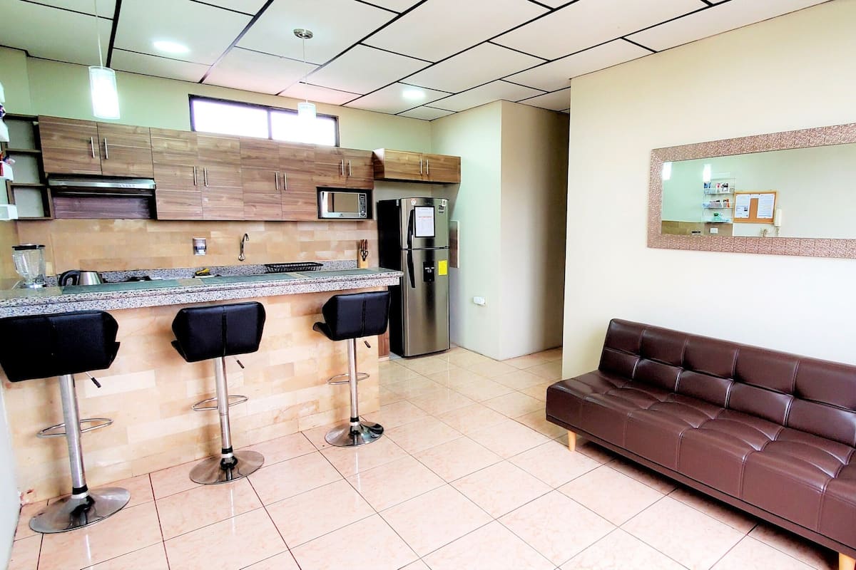 A kitchen with a bar area, a refrigerator, and a brown leather sofa.
