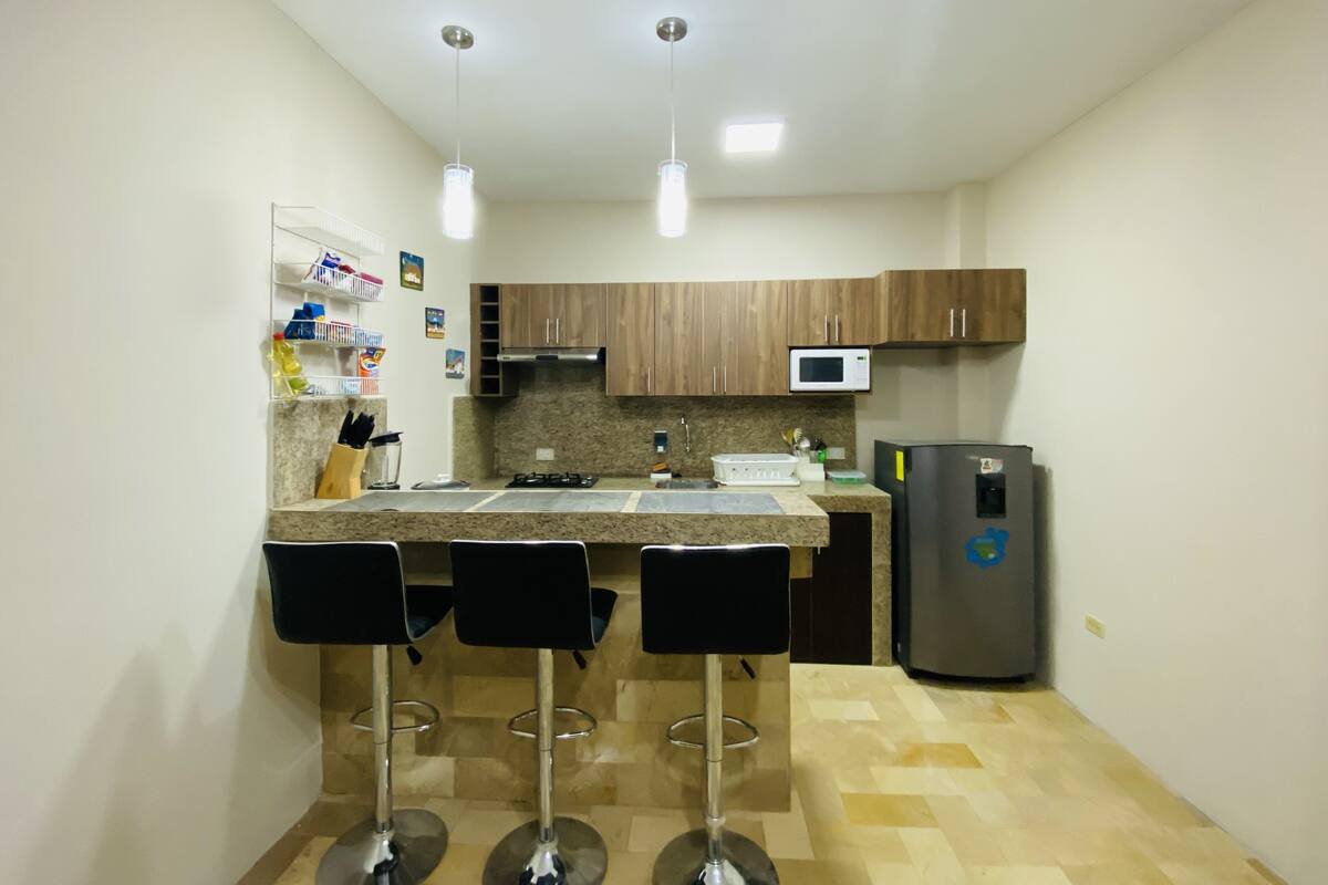 A compact kitchen with a central island, bar stools, a microwave, and a refrigerator.