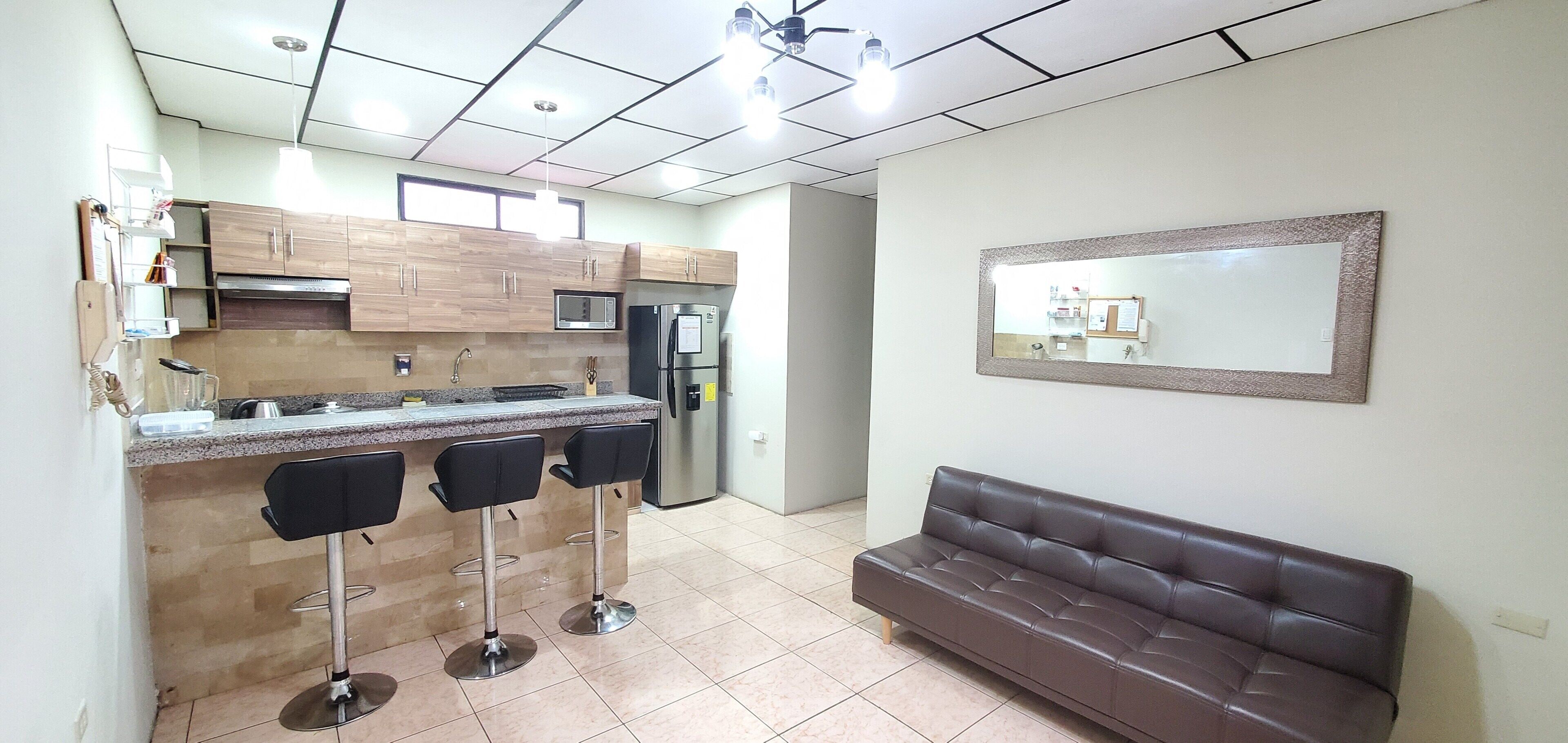 A kitchen with a bar area, a refrigerator, and a brown leather sofa.