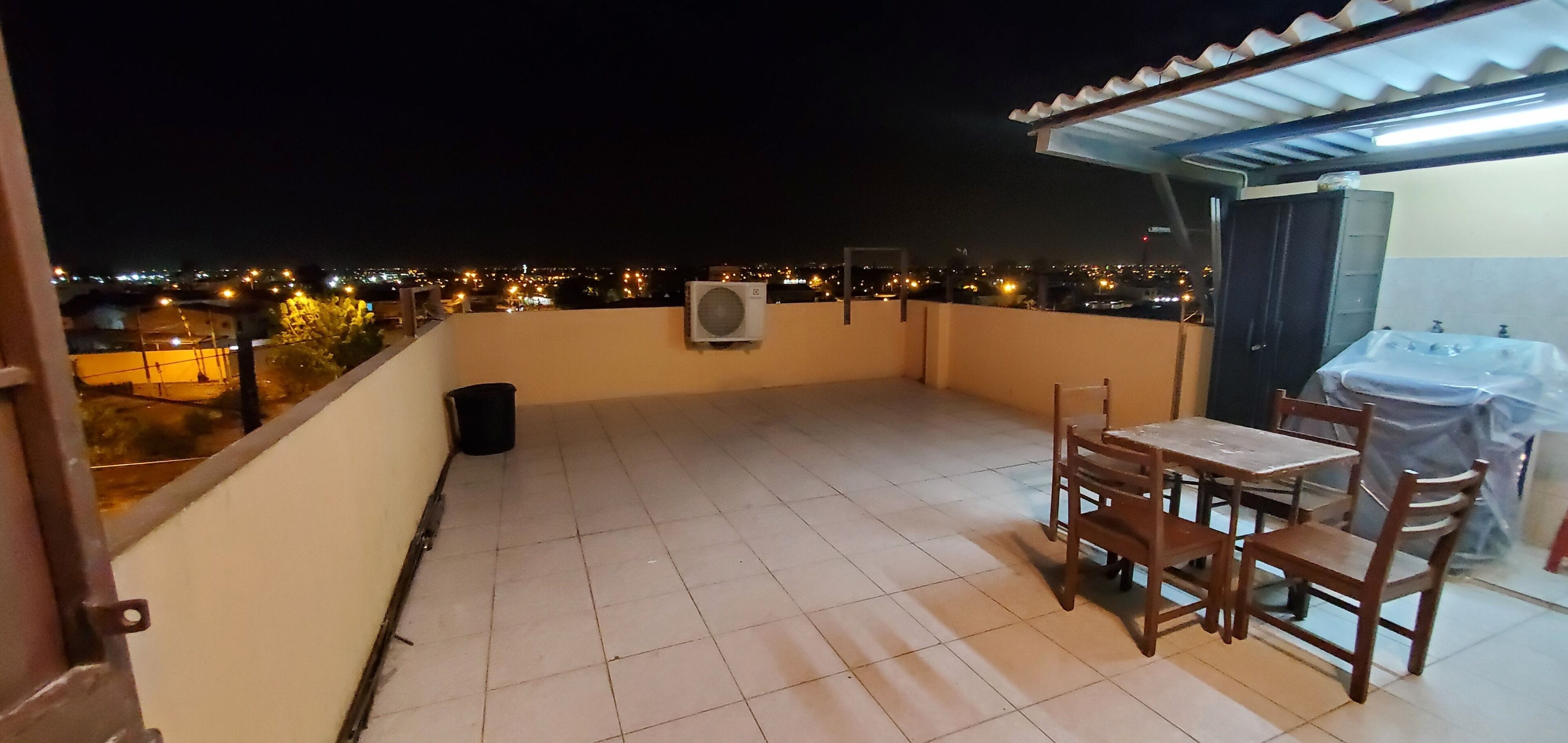 Uma varanda com mesa, cadeiras, uma lixeira e um aparelho de ar condicionado.