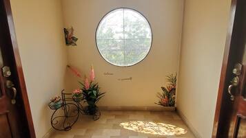 Een hal met een houten deur, een rond raam en decoratieve elementen zoals een fiets en potplanten.