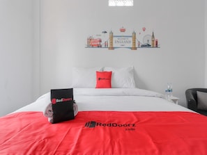Hotelkamer met een bed, kussens, een tas van RedDoorz, een waterfles en een decoratie met bezienswaardigheden van Londen.