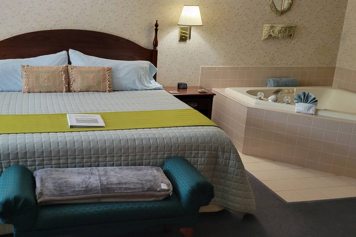 Hotellihuone, jossa on suuri sänky, yöpöytä, sängyn vieressä oleva pöytä, lukuvalo, kylpyammeella varustettu kylpyhuone ja penkki.