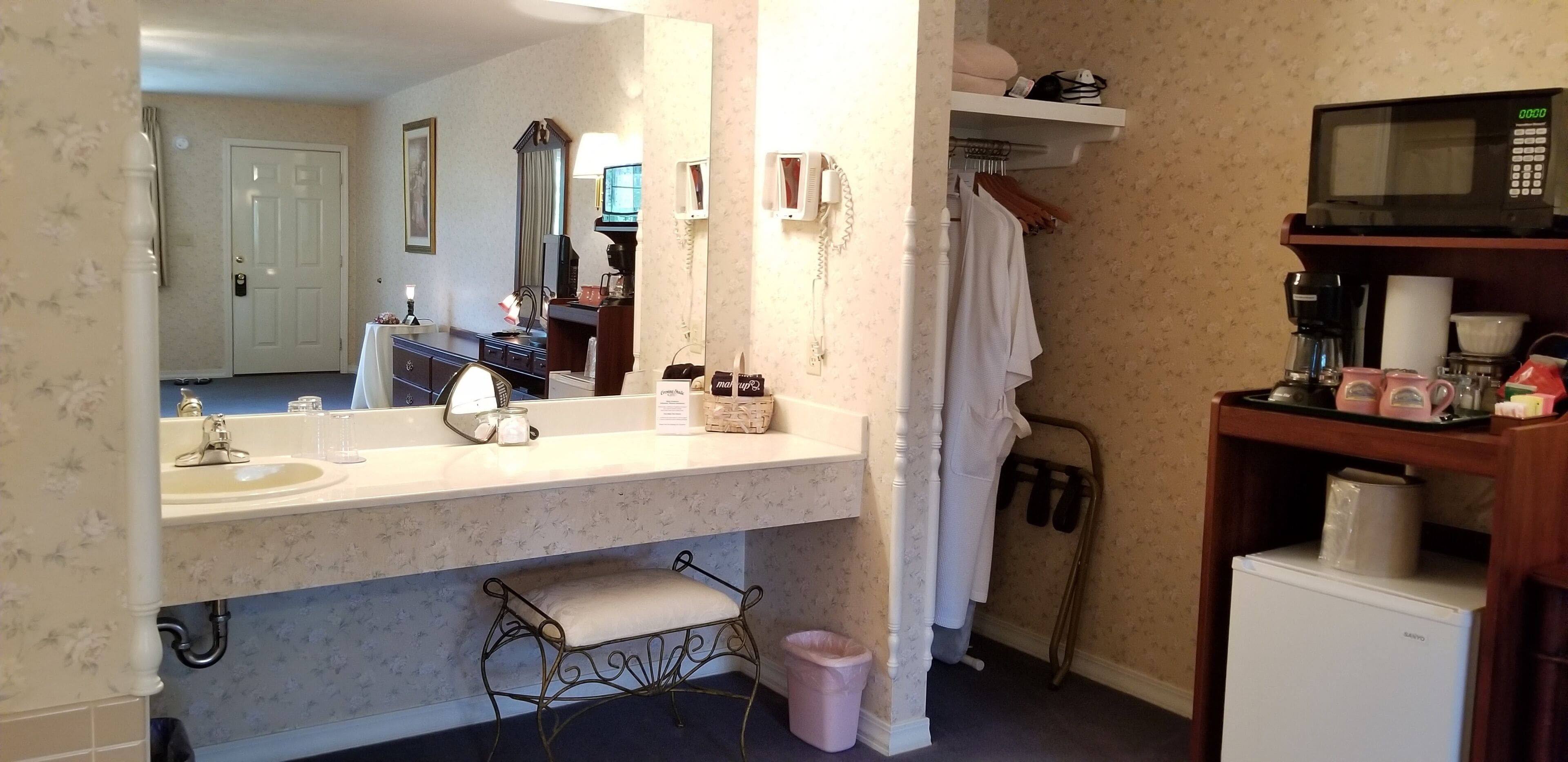Ein Badezimmer mit Waschbecken, Spiegel, Handtuchhalter und einer Mikrowelle auf einem Regal.