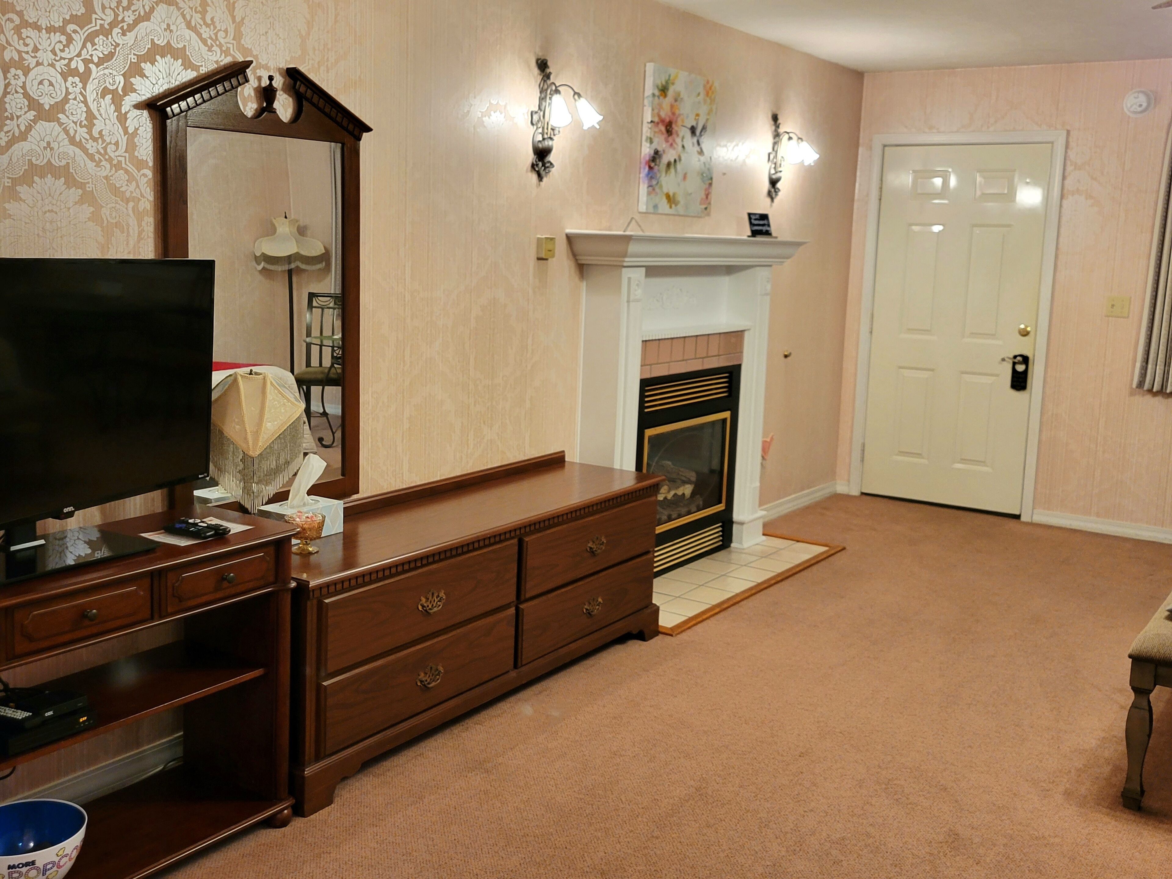 A living room with a television, wooden dresser, fireplace, and a door.