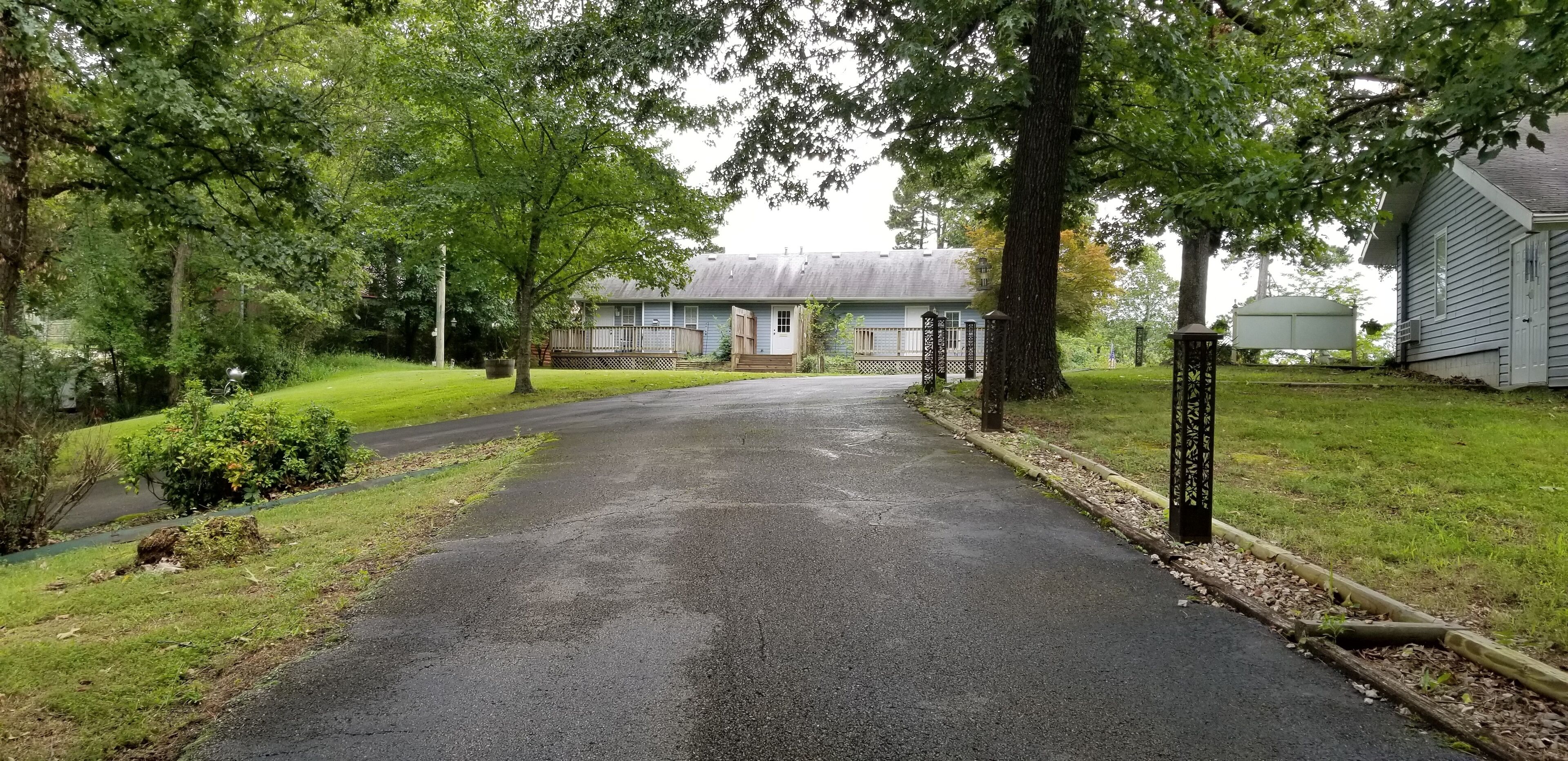 A driveway leading to a building with a covered porch and a small garden area.