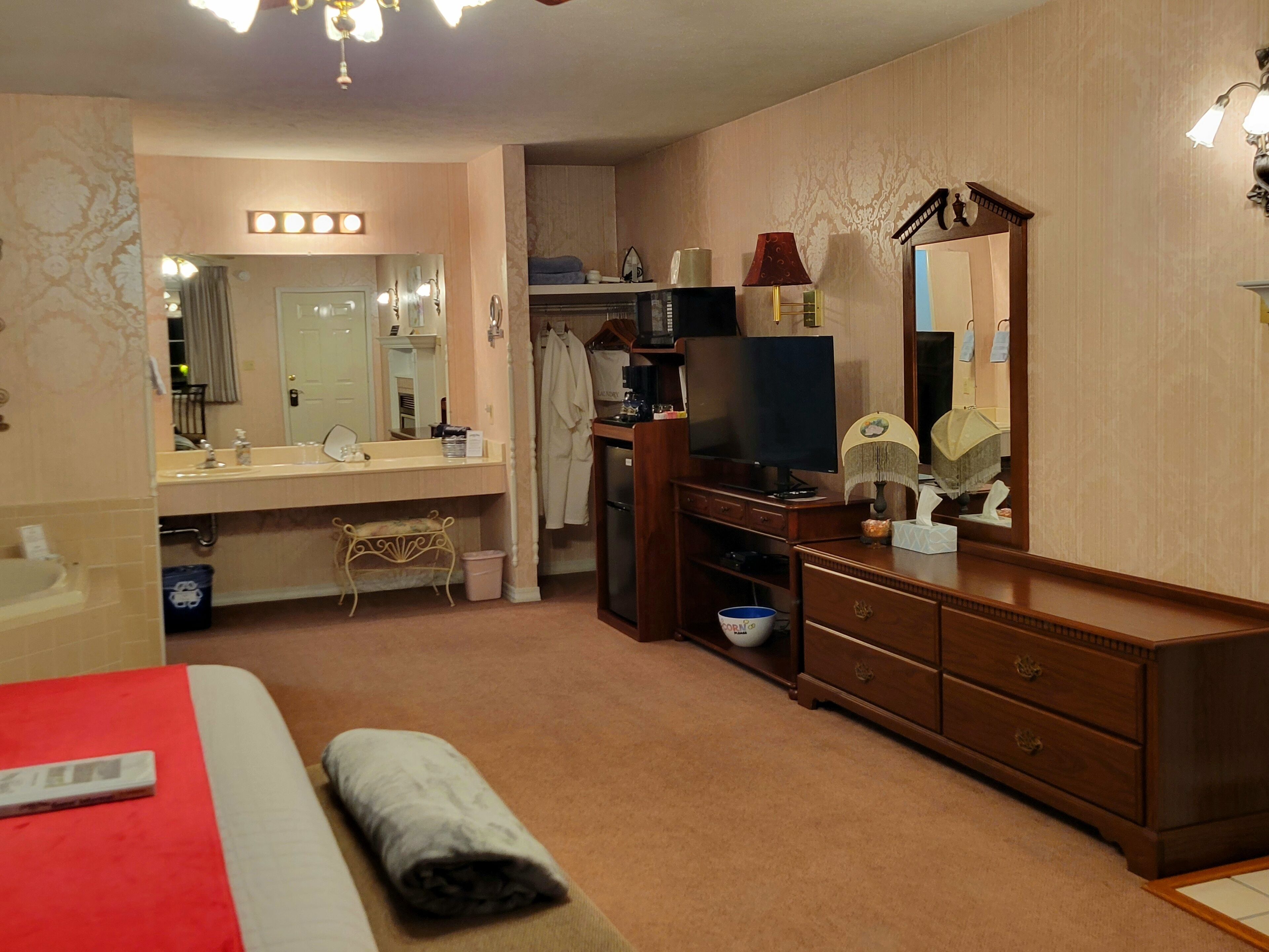 A hotel room with a bed, a TV, a dresser, a mirror, and a bathroom with a sink and mirror.