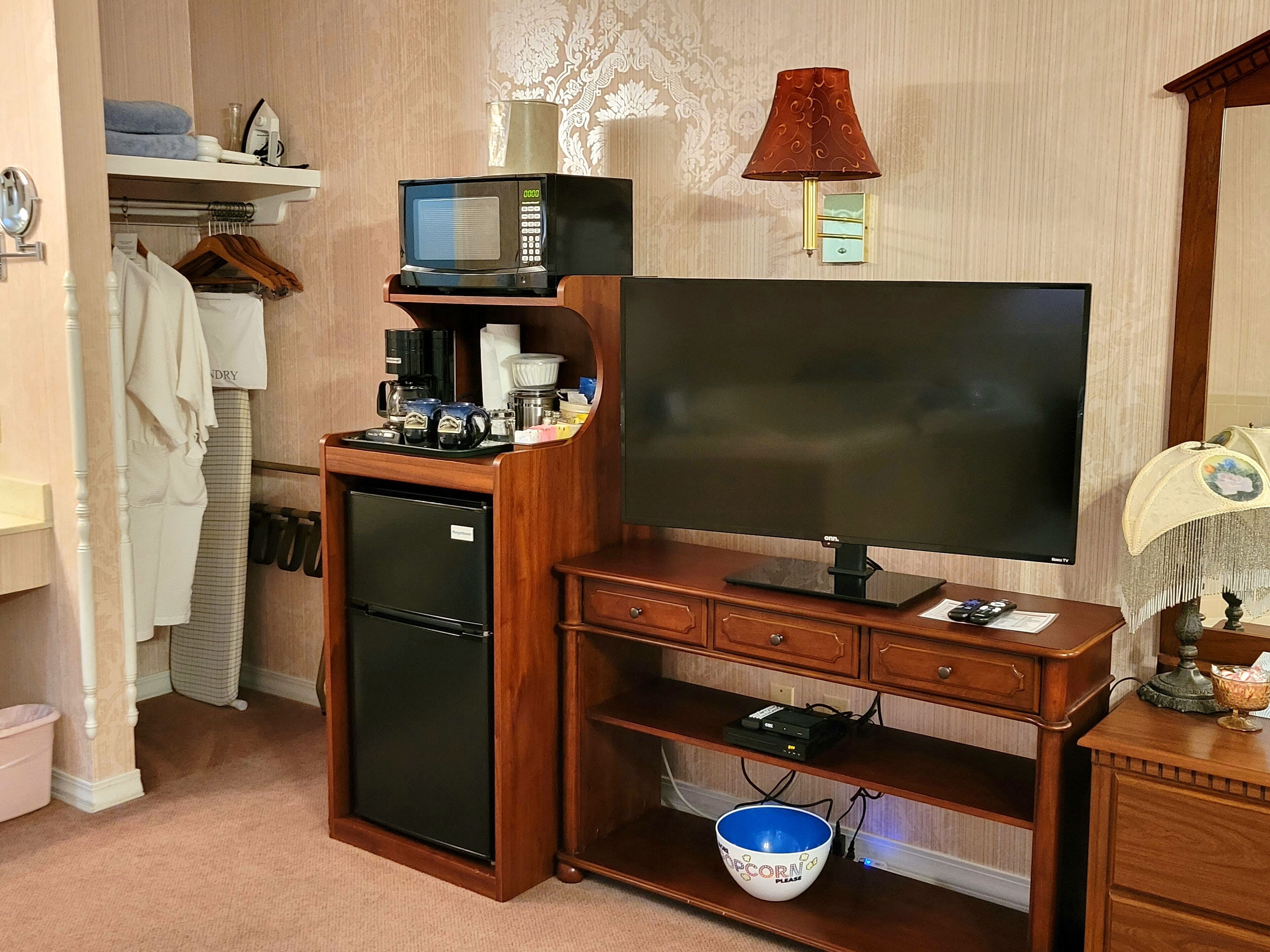 Ein kleines Hotelzimmer mit Schreibtisch aus Holz, Flachbildfernseher, kleinem Kühlschrank und Mikrowelle auf der Arbeitsfläche.