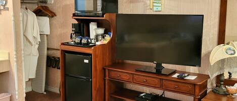 Ein kleines Hotelzimmer mit Schreibtisch aus Holz, Flachbildfernseher, kleinem Kühlschrank und Mikrowelle auf der Arbeitsfläche.