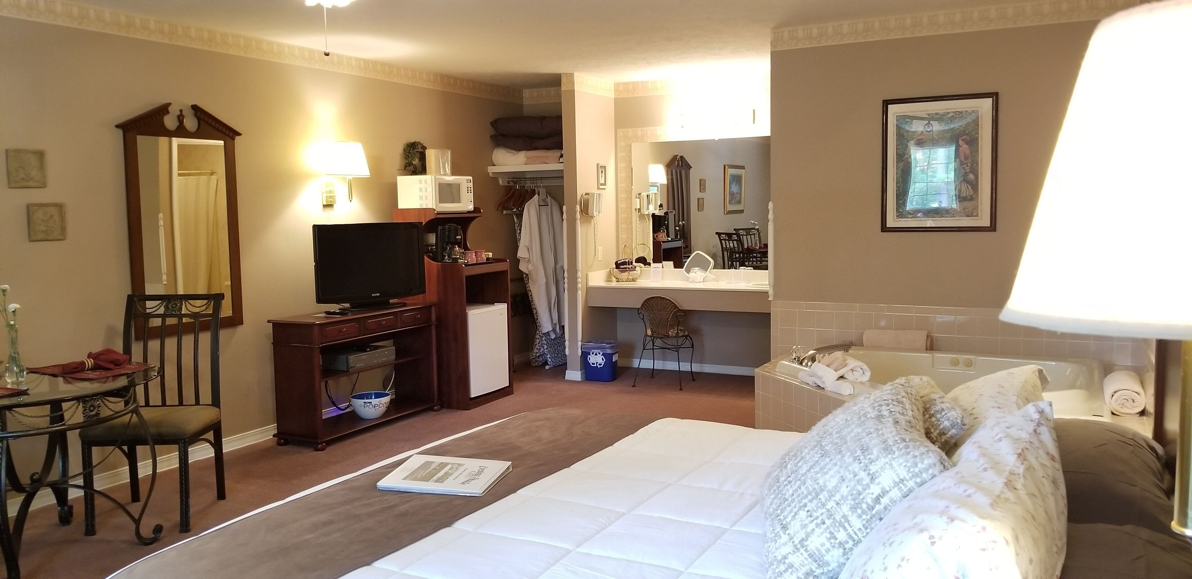 Een hotelkamer met een bed, een bureau met een computer, een televisie, een magnetron en een badkamer met een wastafel en spiegel.
