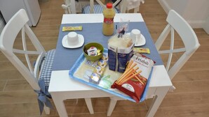Ein Esstisch mit blauer Tischdecke, weißen Stühlen und verschiedenen Speisen, darunter Brot, Gewürze und eine Senflasche.