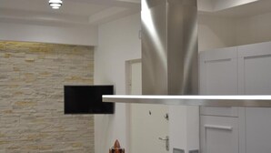 Eine moderne Küche mit Steinrückwand, Edelstahlmöbeln und einem an der Wand befestigten Flachbildfernseher.