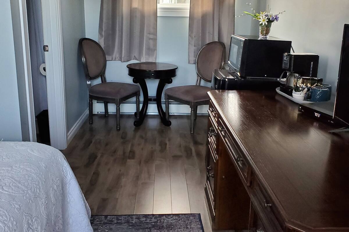 A hotel room with a bed, a desk, a chair, a small table, a television, and a window with curtains.