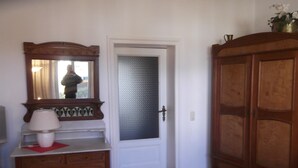 Een kamer met een houten kast, een spiegel, een dressoir en een deur met een geëtst glaspaneel.