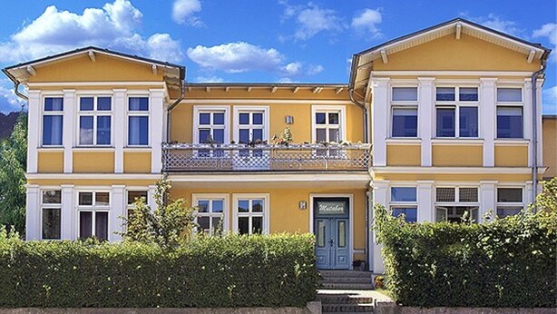 Een gebouw met twee verdiepingen, een gele gevel, witte details en een balkon met een hekwerk.
