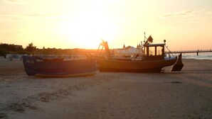 Twee boten op een zandstrand met een ondergaande zon op de achtergrond.