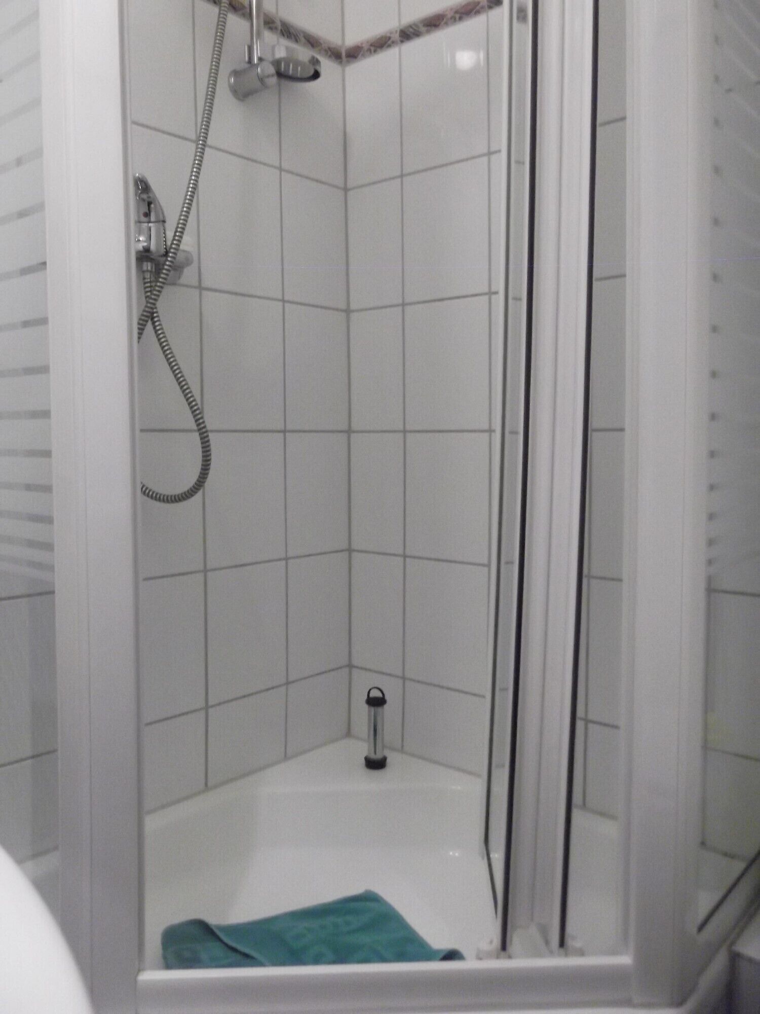 Un espacio de ducha pequeño y cerrado, con puerta de vidrio, ducha de mano y grifo de mano.