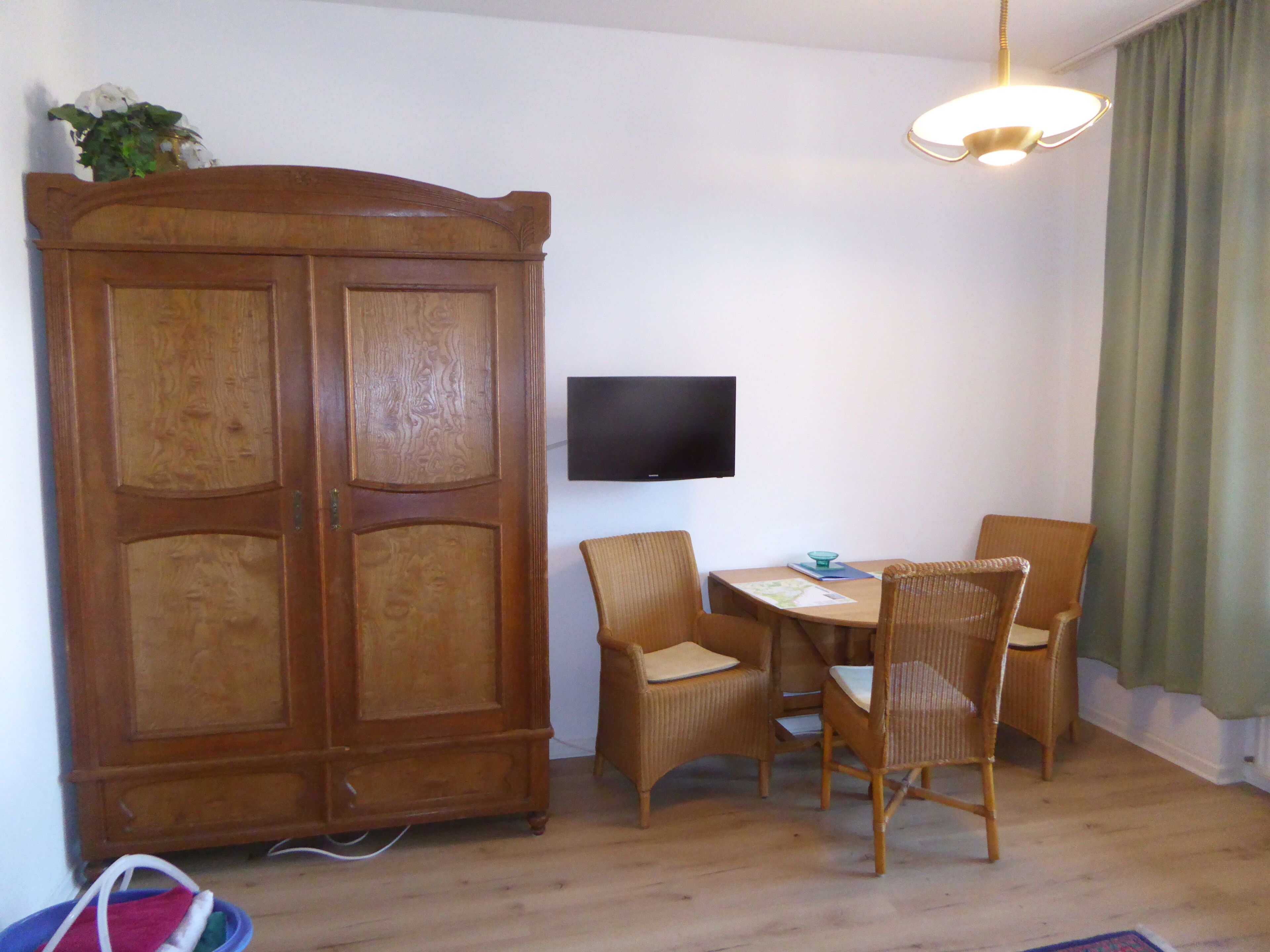 Um quarto com um armário de madeira, uma televisão e uma mesa de jantar com cadeiras.