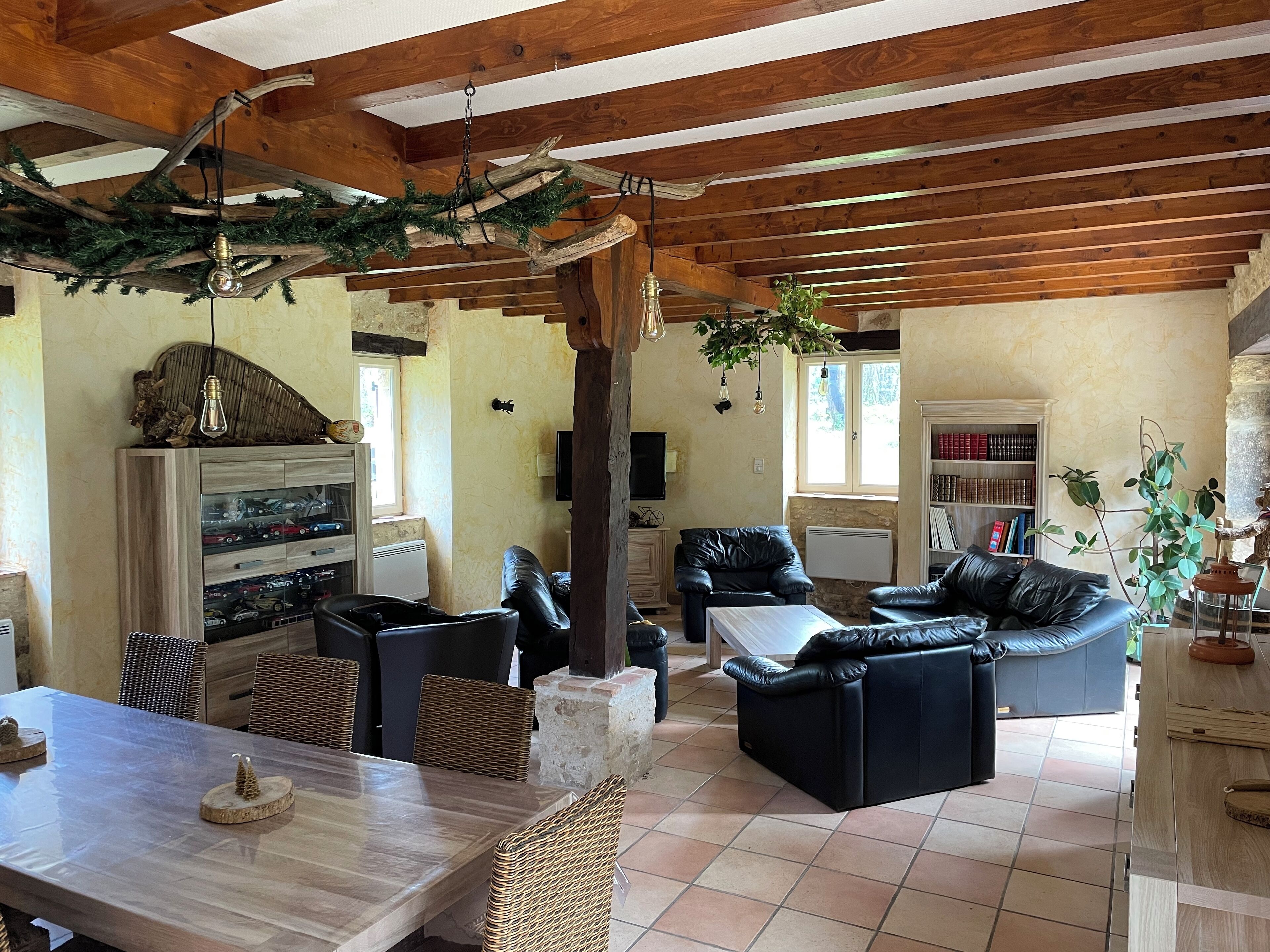 A spacious living area with a wooden ceiling, a dining table with wicker chairs, and a black leather sofa.