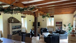 A spacious living area with a wooden ceiling, a dining table with wicker chairs, and a black leather sofa.