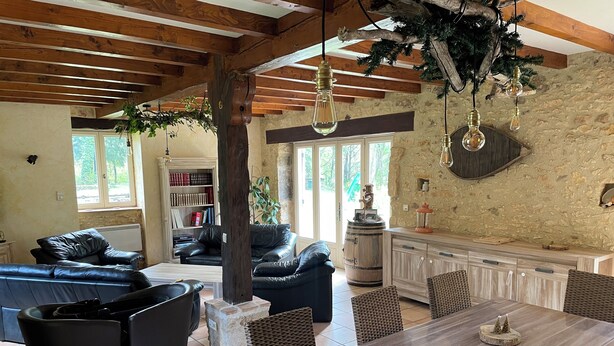 A spacious living area with a wooden ceiling, a large dining table, and black leather sofas.