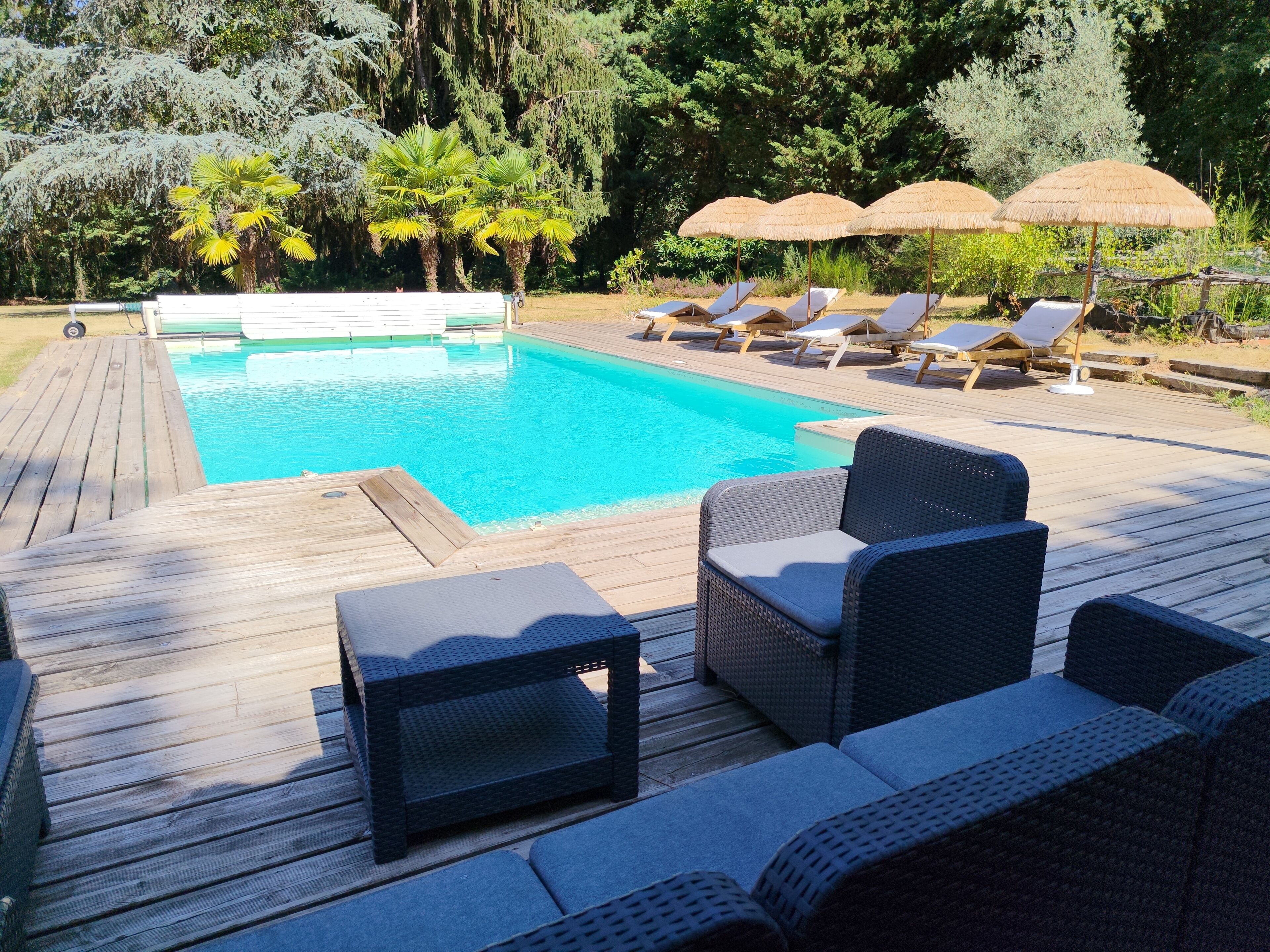 Eine Holzterrasse mit Pool, Liegestühlen und Sonnenschirmen.